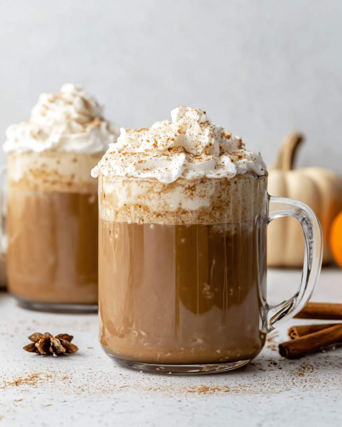 Glass mugs filled with Pumpkin Spice Latte topped with whipped cream and a sprinkle of cinnamon.