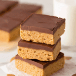 Stack of three no-bake peanut butter bars with a smooth chocolate topping on parchment paper.