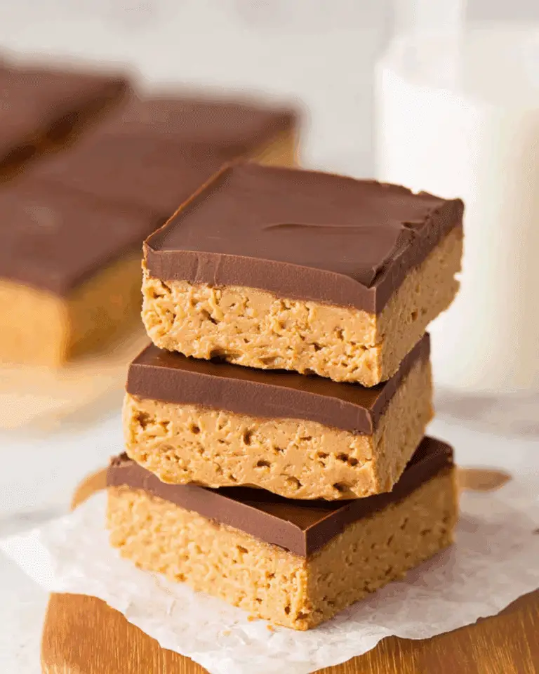Stack of three no-bake peanut butter bars with a smooth chocolate topping on parchment paper.