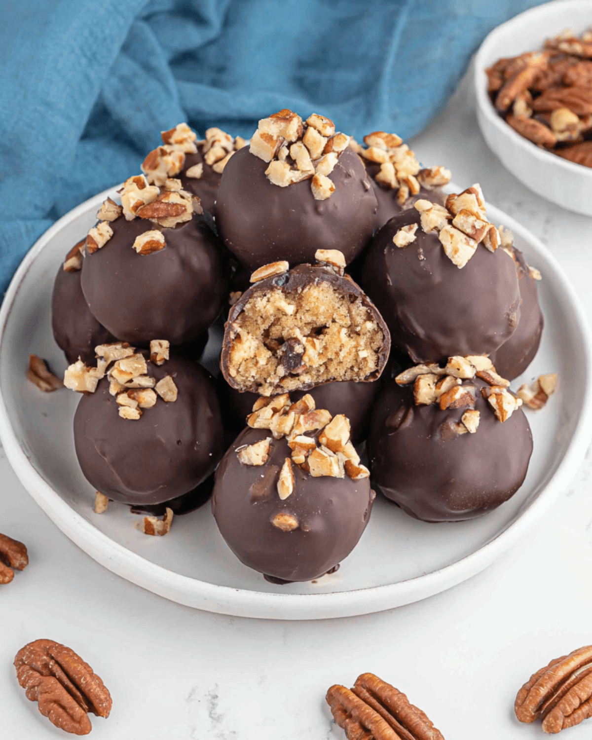 Pecan pie balls coated in chocolate, topped with chopped pecans, and filled with a soft pecan and cookie mixture.