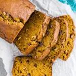 A loaf of pumpkin banana bread sliced on parchment paper, showing a moist texture with chocolate chips and seeds.