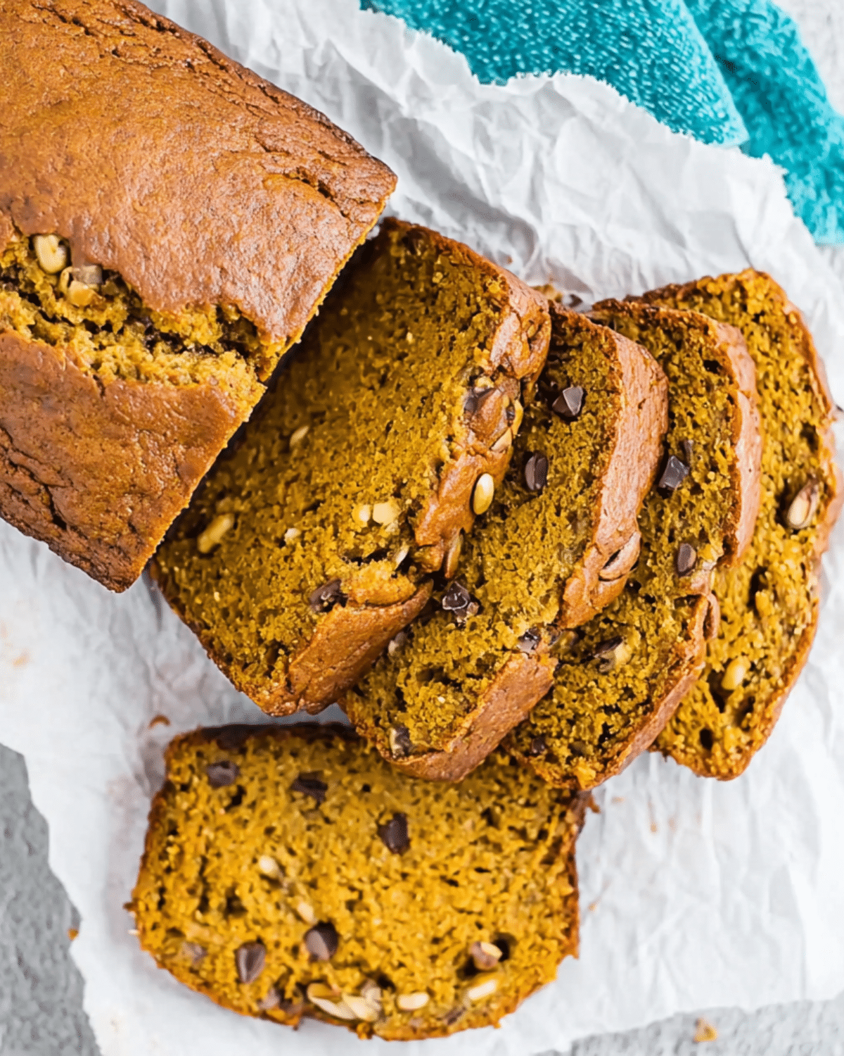 A loaf of pumpkin banana bread sliced on parchment paper, showing a moist texture with chocolate chips and seeds.