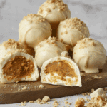 Pumpkin cheesecake balls coated in white chocolate and sprinkled with crushed graham crackers, with one cut open to reveal a creamy pumpkin center.