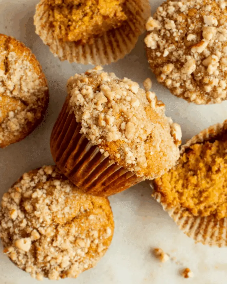 Pumpkin Coffee Cake Muffins topped with crumbly streusel, arranged on a light surface.