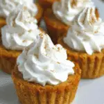 Pumpkin pie cupcakes topped with swirls of whipped cream and sprinkled with cinnamon, served on a white plate.
