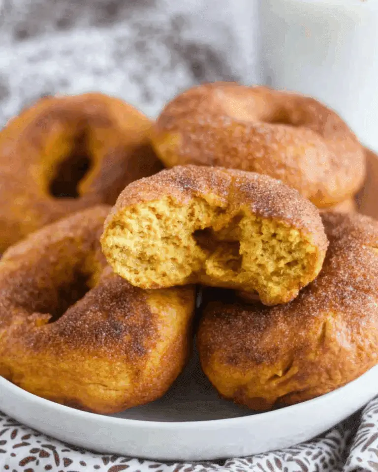 A plate of Pumpkin Sourdough Bagels coated in cinnamon sugar, with one showing a fluffy bite taken out.
