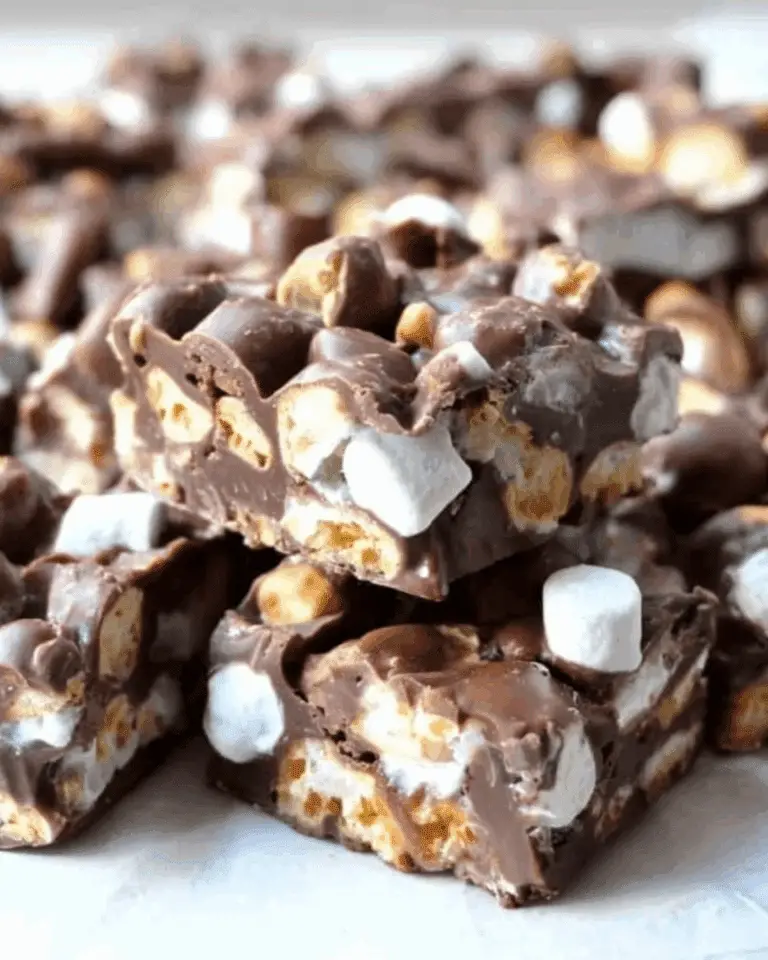 Close-up of homemade ROCKY ROAD CANDY with chocolate, marshmallows, and peanuts stacked on parchment paper.