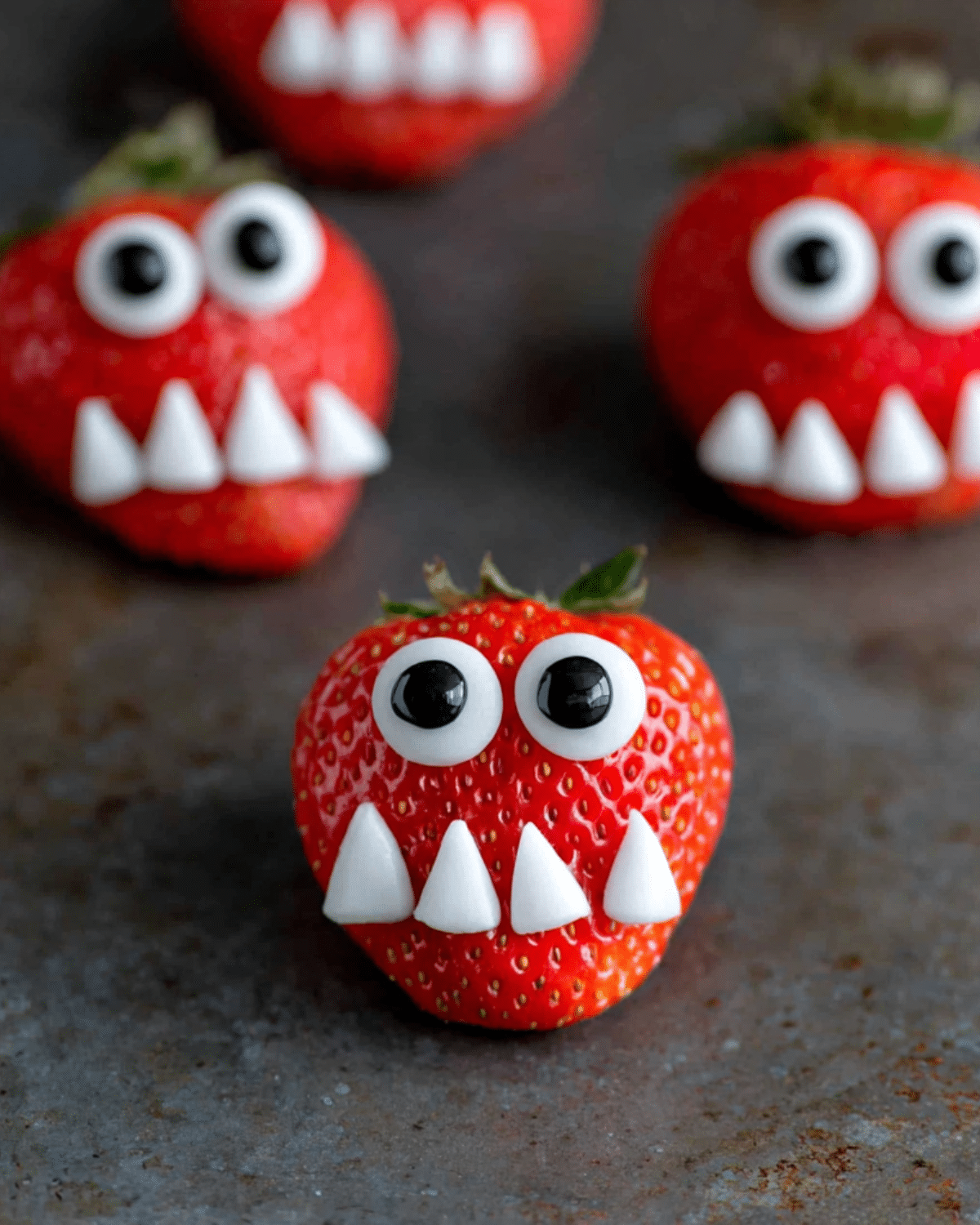 Fresh strawberries decorated as Strawberry Monsters with candy eyes and pointed white candy teeth.