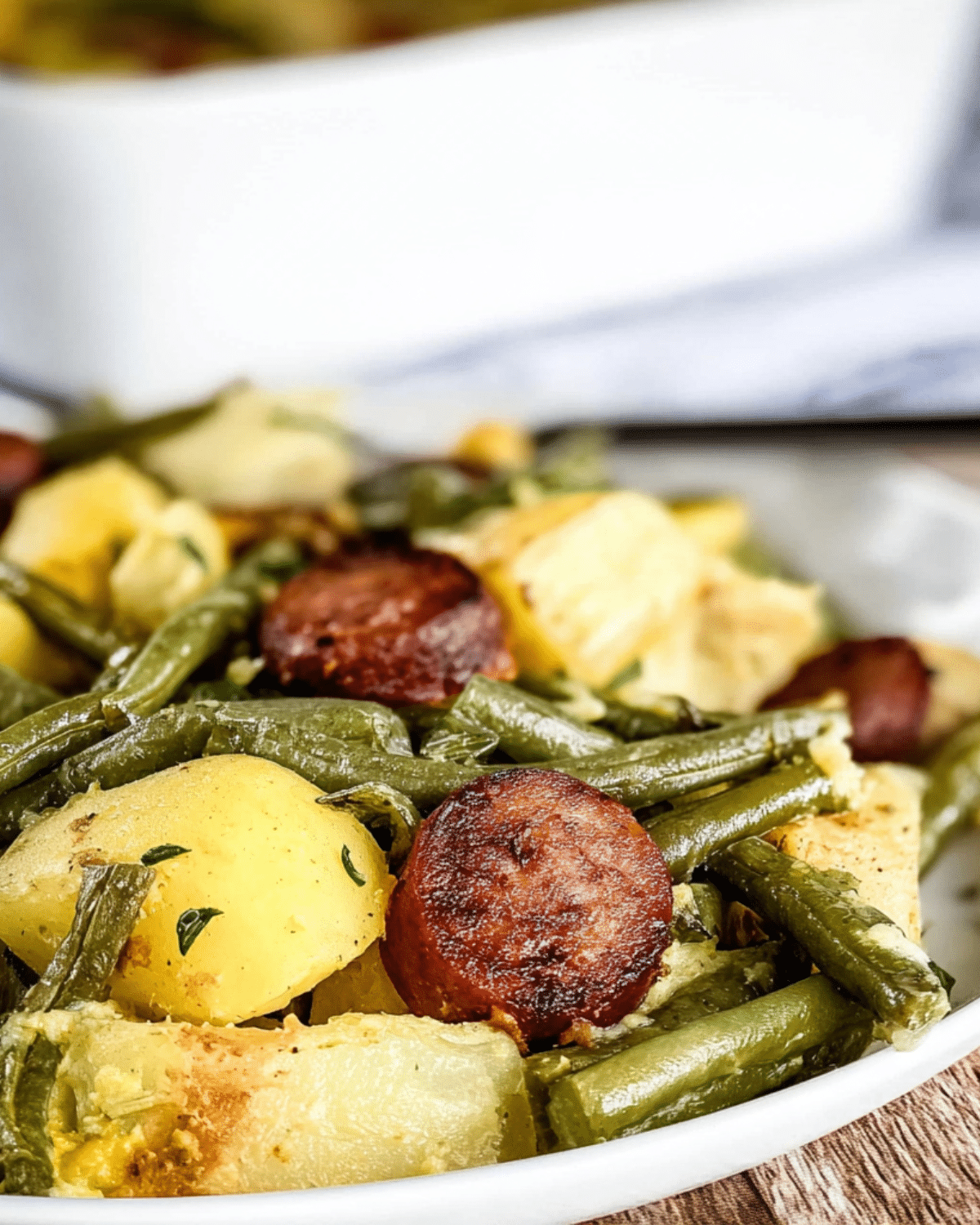 Sausage green bean potato casserole with golden potatoes, tender green beans, and slices of browned sausage served in a white dish.
