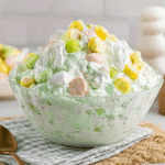 Glass bowl filled with fluffy seafoam salad made with whipped topping, pastel marshmallows, and crushed pineapple, topped with colorful candies.