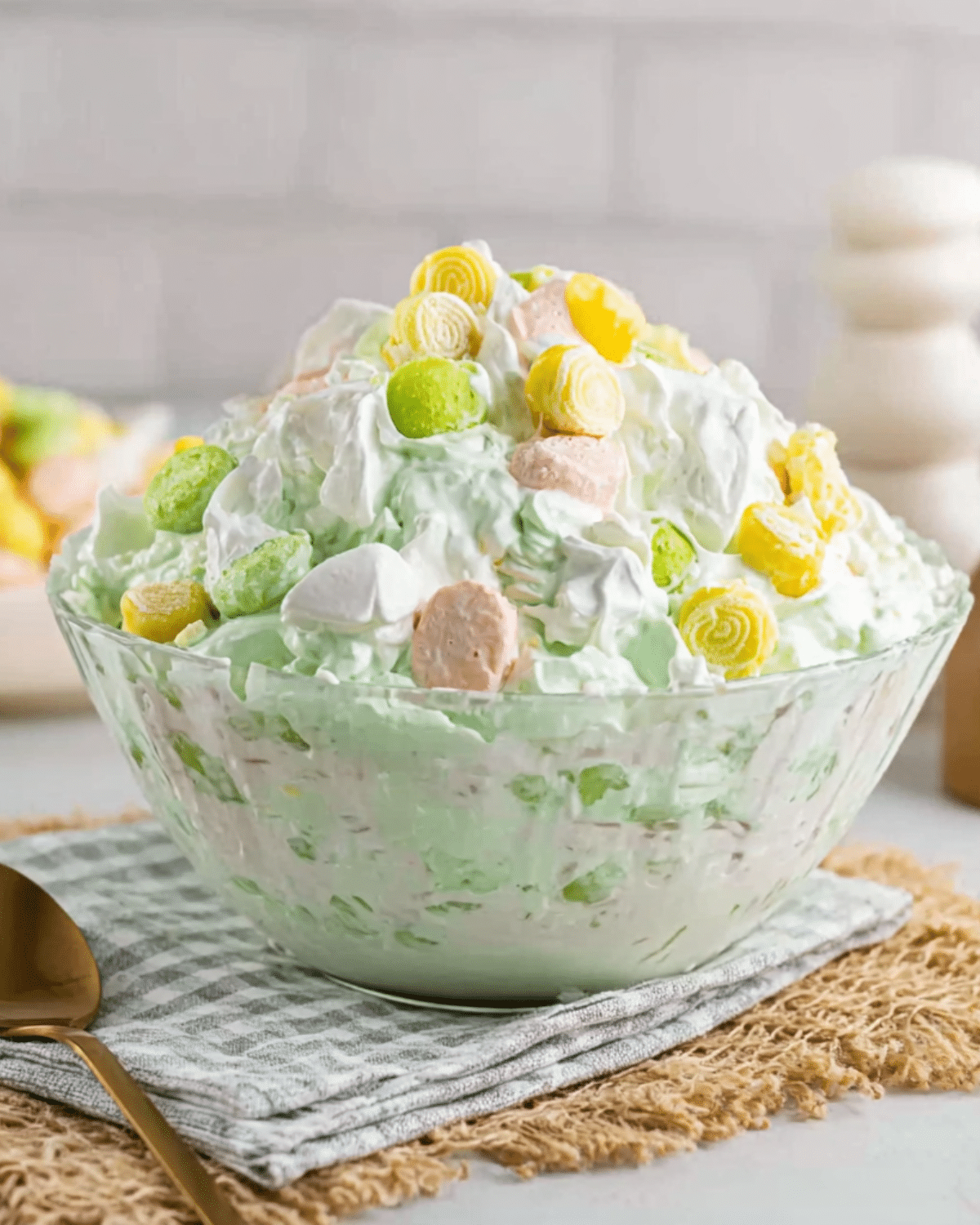 Glass bowl filled with fluffy seafoam salad made with whipped topping, pastel marshmallows, and crushed pineapple, topped with colorful candies.