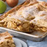 Sheet Pan Apple Pie with a golden, flaky crust and cinnamon-spiced apple filling, served with a slice on a white plate.