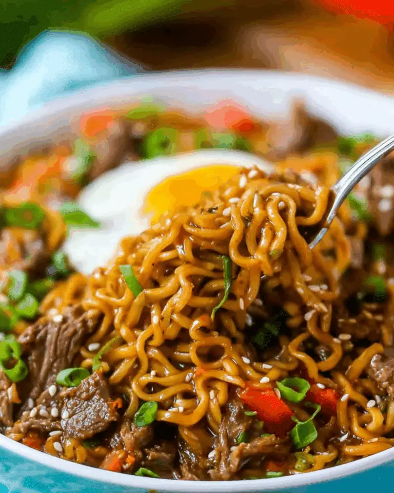 A close-up of Slow Cooker Beef Ramen topped with green onions, sesame seeds, and a soft-cooked egg.