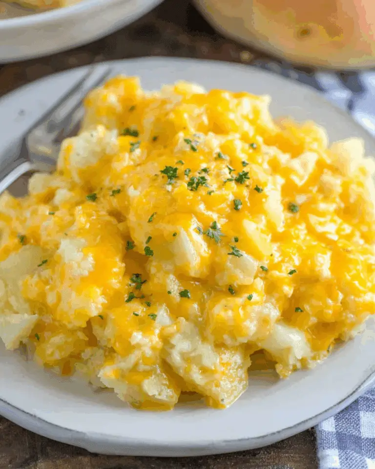 Plate of Slow Cooker Cheesy Potatoes topped with melted cheddar cheese and garnished with fresh parsley.