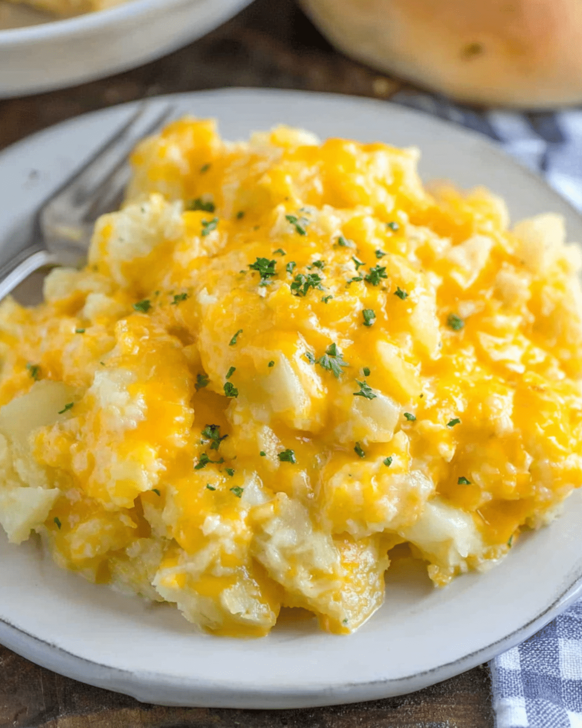 Plate of Slow Cooker Cheesy Potatoes topped with melted cheddar cheese and garnished with fresh parsley.