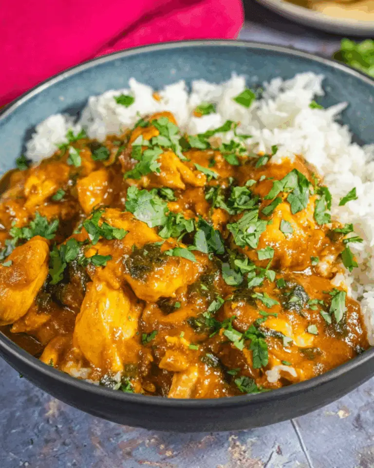 Slow Cooker Coconut Curry Chicken served with white rice and garnished with fresh cilantro in a black bowl.