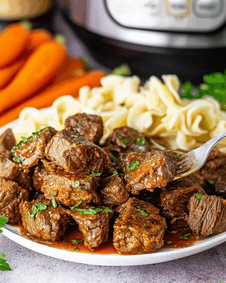 Plate of tender Slow Cooker Steak Bites in savory sauce, served with egg noodles and carrots.