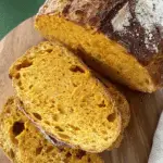 A loaf of Soft Pumpkin Sourdough Bread with golden-orange slices showing its airy texture and rustic crust.