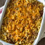Baked sour cream casserole with layers of egg noodles, ground beef, tomato sauce, and melted cheddar cheese in a white dish.