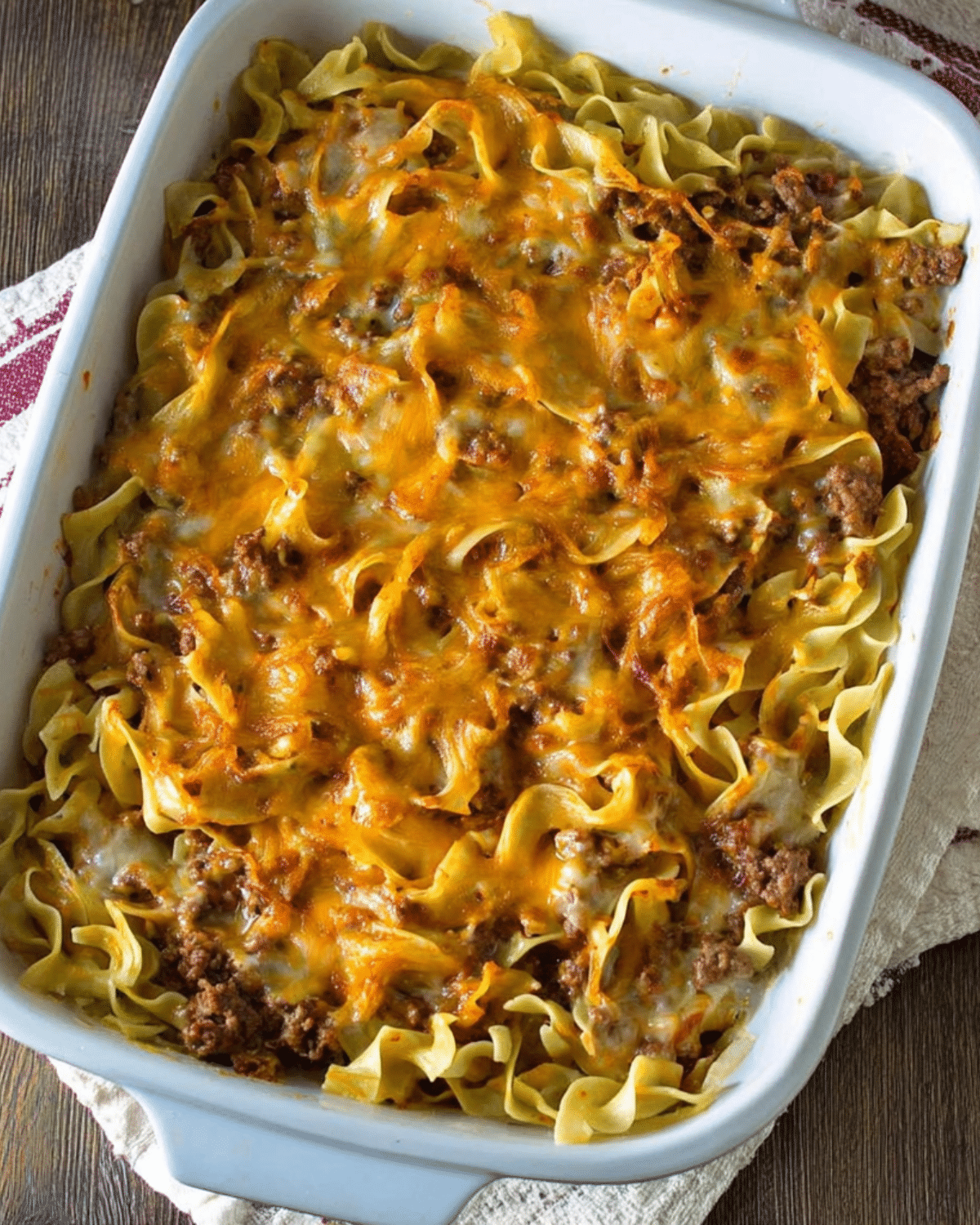 Baked sour cream casserole with layers of egg noodles, ground beef, tomato sauce, and melted cheddar cheese in a white dish.