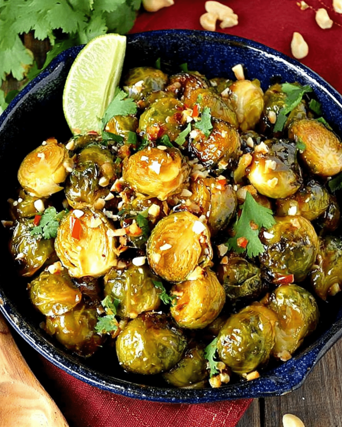 A bowl of Sweet Chili Brussel Sprouts garnished with chopped peanuts, cilantro, and a wedge of lime.