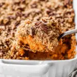 Sweet potato casserole topped with a pecan crumble being scooped from a white baking dish.