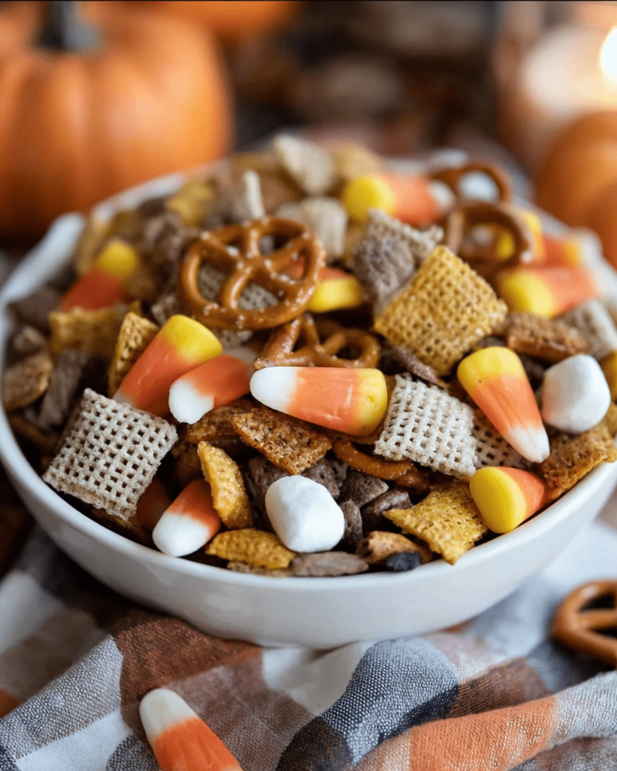 A bowl of Sweet and Salty Fall Snack Mix featuring candy corn, pretzels, Chex cereal, marshmallows, and chocolate pieces.