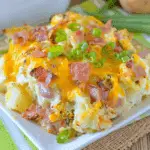 Serving of twice baked potato casserole topped with melted cheddar cheese, crispy bacon, and sliced green onions.