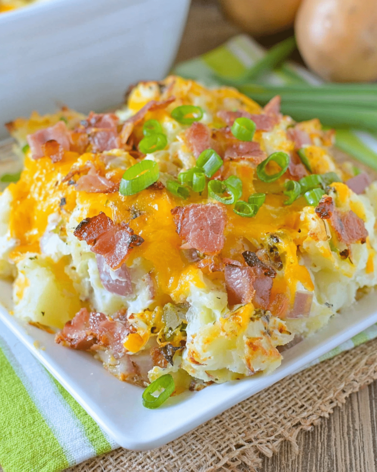 Serving of twice baked potato casserole topped with melted cheddar cheese, crispy bacon, and sliced green onions.