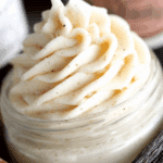 Close-up of creamy Vanilla Bean Buttercream piped into a swirl in a glass jar, with visible vanilla bean specks.