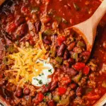 Wendy's Chili Recipe featuring ground beef, kidney beans, tomatoes, and bell peppers, topped with shredded cheese, sour cream, and parsley in a large pot.