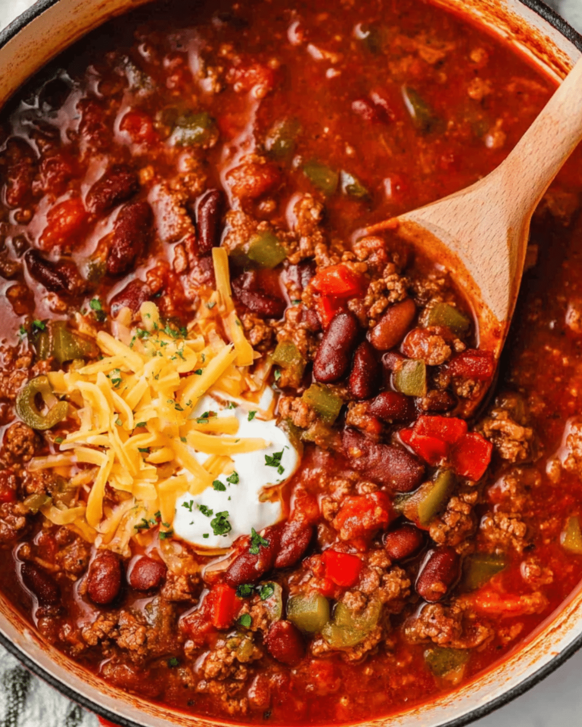 Wendy's Chili Recipe featuring ground beef, kidney beans, tomatoes, and bell peppers, topped with shredded cheese, sour cream, and parsley in a large pot.