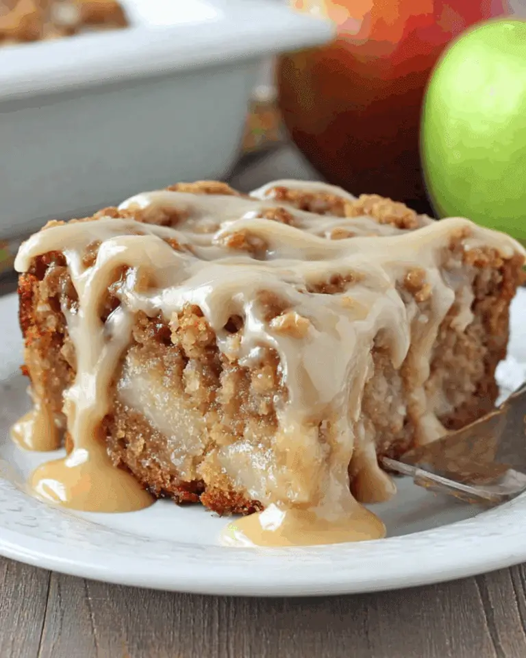 A slice of apple dapple cake drizzled with rich caramel glaze on a white plate.