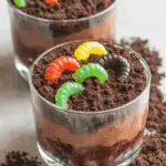 Glass cups filled with layered chocolate pudding, crushed cookies, and gummy worms to create festive Halloween Dirt Cups.