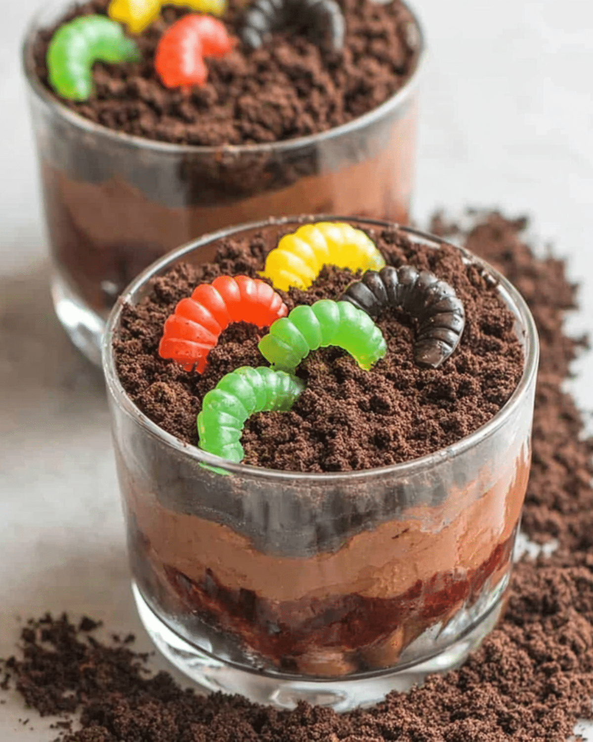 Glass cups filled with layered chocolate pudding, crushed cookies, and gummy worms to create festive Halloween Dirt Cups.