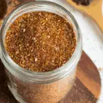 Glass jar filled with homemade taco seasoning, a blend of chili powder, paprika, garlic, and spices, on a wooden board.