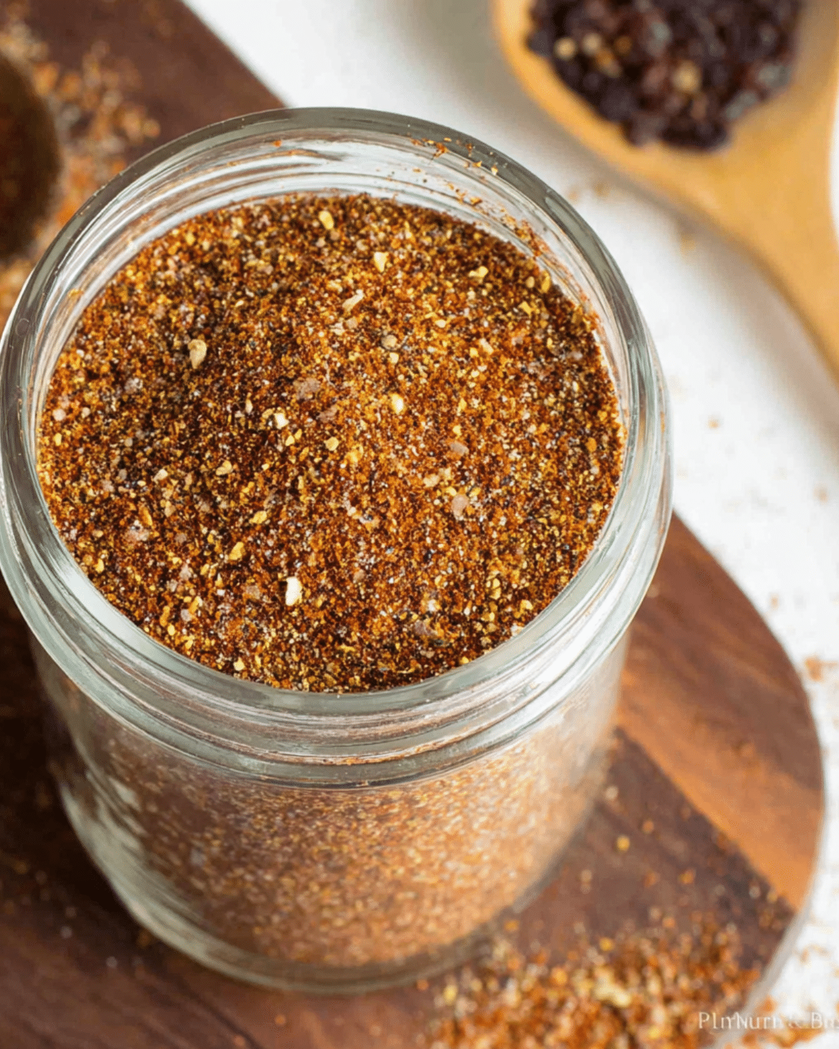 Glass jar filled with homemade taco seasoning, a blend of chili powder, paprika, garlic, and spices, on a wooden board.