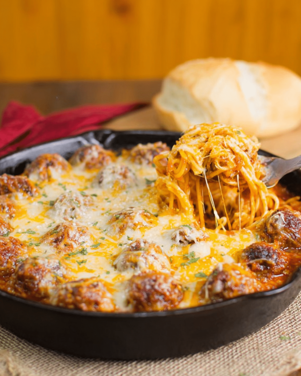 Cheesy Baked Spaghetti Meatballs in a cast iron skillet with melted cheese and marinara, served with bread.