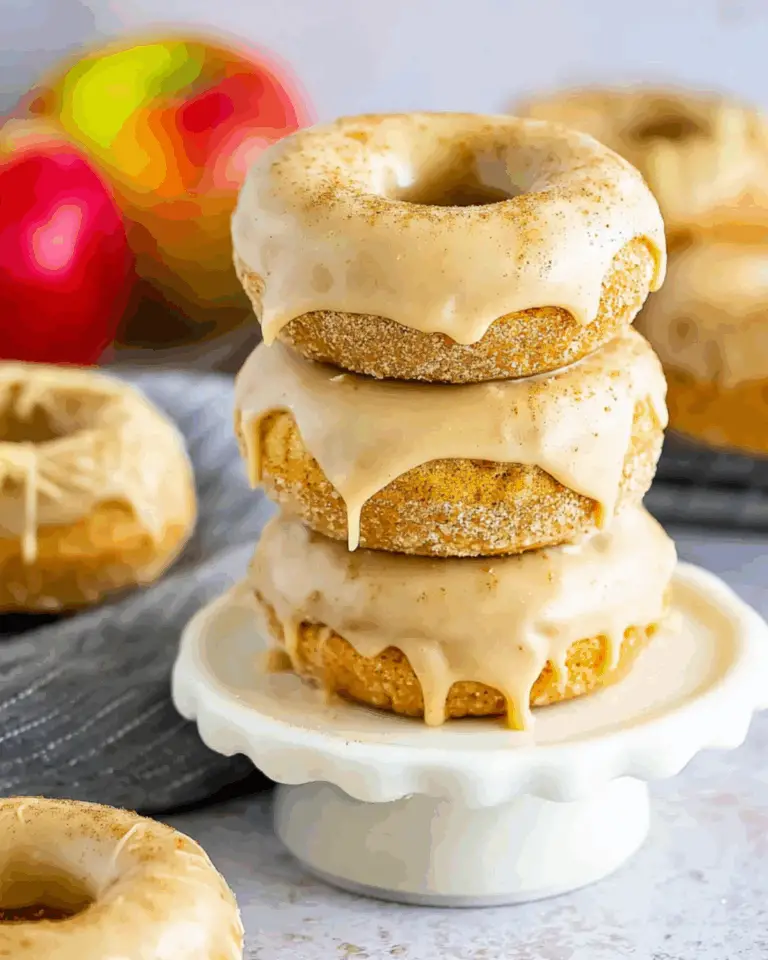Stack of baked apple cider doughnuts with cinnamon maple glaze on a white pedestal stand.