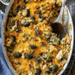 Broccoli cheddar chicken and rice casserole baked in a white oval dish, topped with melted cheddar cheese and fresh herbs.