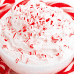 Creamy white Candy Cane Dip topped with crushed candy canes in a white bowl, surrounded by whole candy canes.