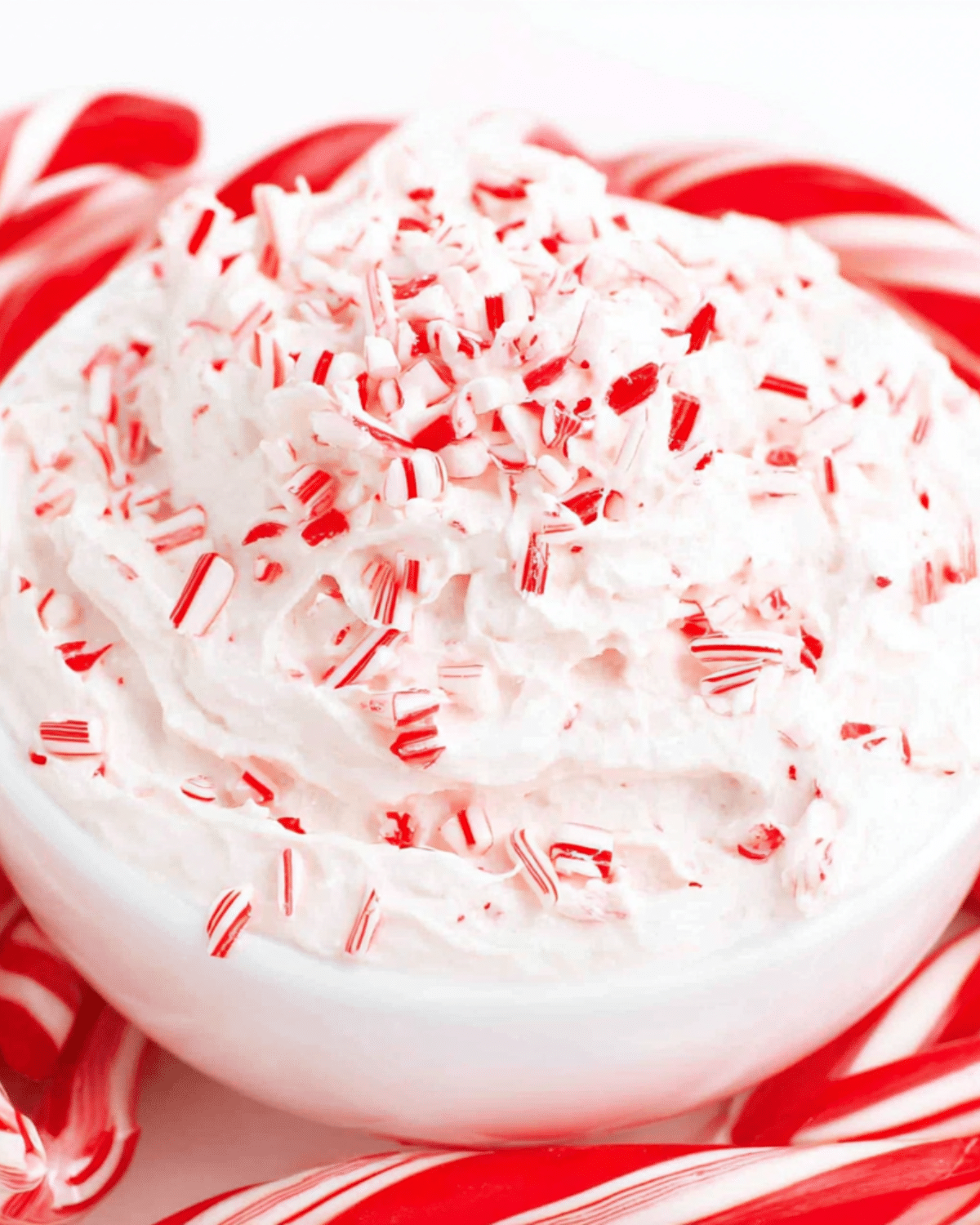 Creamy white Candy Cane Dip topped with crushed candy canes in a white bowl, surrounded by whole candy canes.
