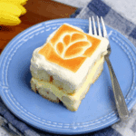 Slice of Chessman banana pudding on a blue plate, showing layers of creamy pudding, bananas, and soft cookies topped with whipped cream and a toasted design.