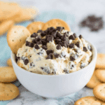 Creamy Cookie Dough Dip topped with chocolate chips in a white bowl, surrounded by round butter crackers.