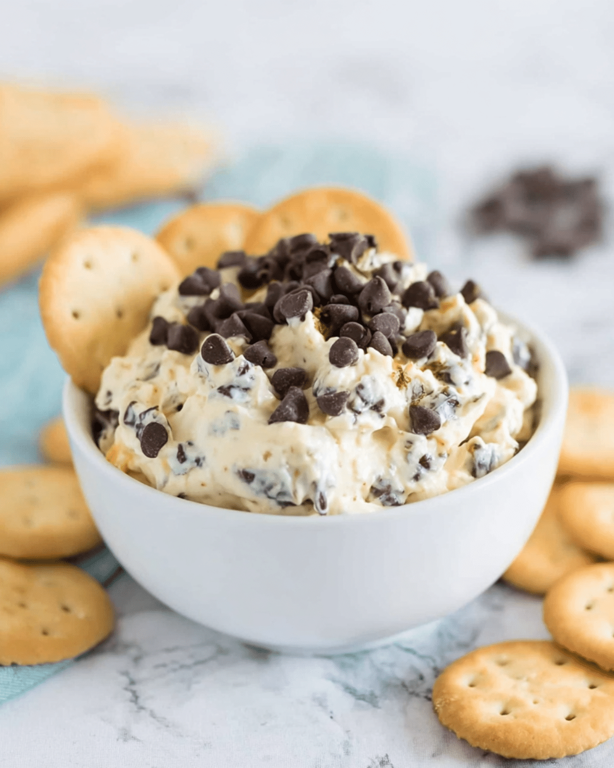 Creamy Cookie Dough Dip topped with chocolate chips in a white bowl, surrounded by round butter crackers.