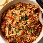 Shredded crockpot salsa chicken garnished with chopped cilantro in a bowl, with tortilla chips on the side.