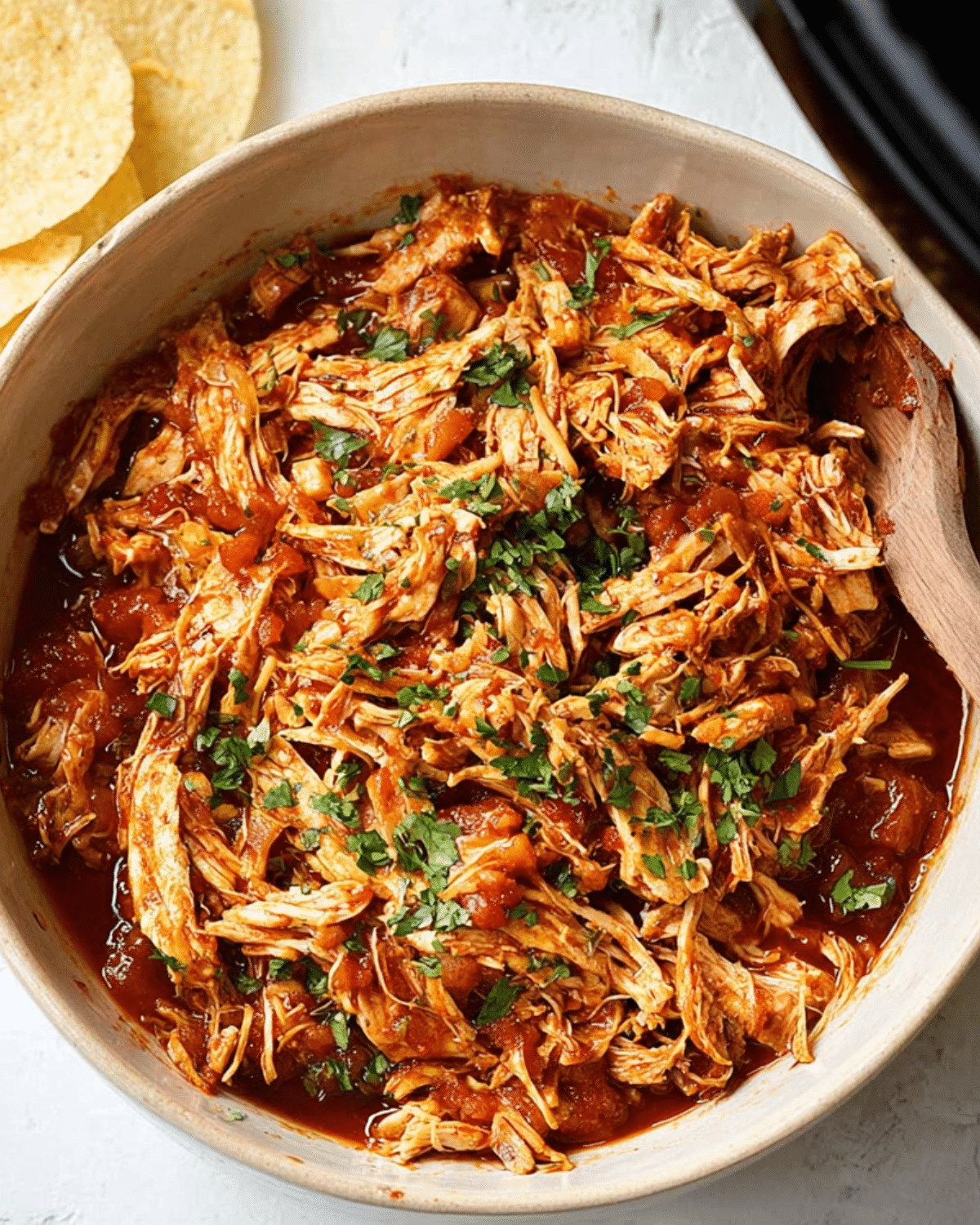 Shredded crockpot salsa chicken garnished with chopped cilantro in a bowl, with tortilla chips on the side.