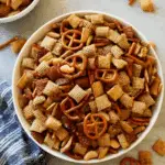 A bowl filled with Chex party mix, including pretzels, mixed Chex cereals, nuts, and seasoning.