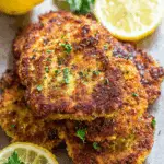 Golden brown chicken cutlets garnished with fresh parsley and served with lemon slices.