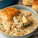 Bowl of creamy chicken pot pie soup with vegetables and a golden biscuit on top